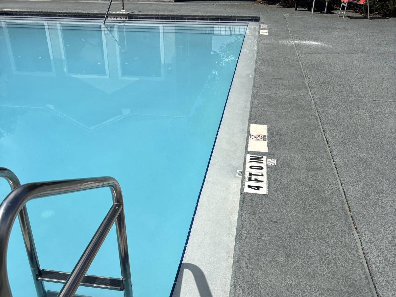 Refinished community pool with a stainless handrail and depth marker