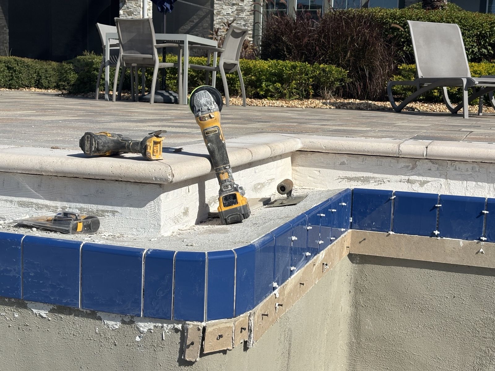 New blue waterline tile being set on a commercial pool, with tools on the coping
